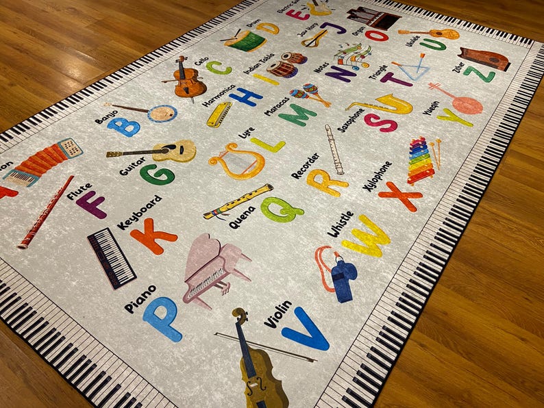 May include: A light gray educational rug featuring the alphabet and musical instruments. The rug has a piano key border and includes illustrations of a piano, violin, guitar, and other instruments. Colorful letters and instrument names are scattered across the rug.
