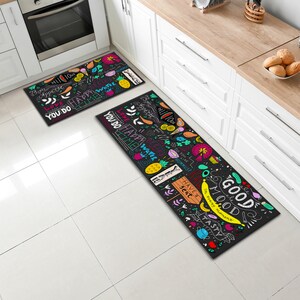 May include: Two black kitchen rugs with colourful, hand-drawn designs and phrases like "You do happy water time", "Good mood", and "Have a seat".