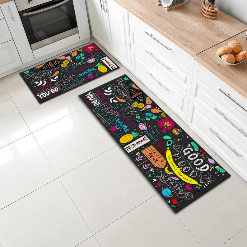 May include: Two black kitchen rugs with colourful, hand-drawn designs and phrases like "You do happy water time", "Good mood", and "Have a seat".