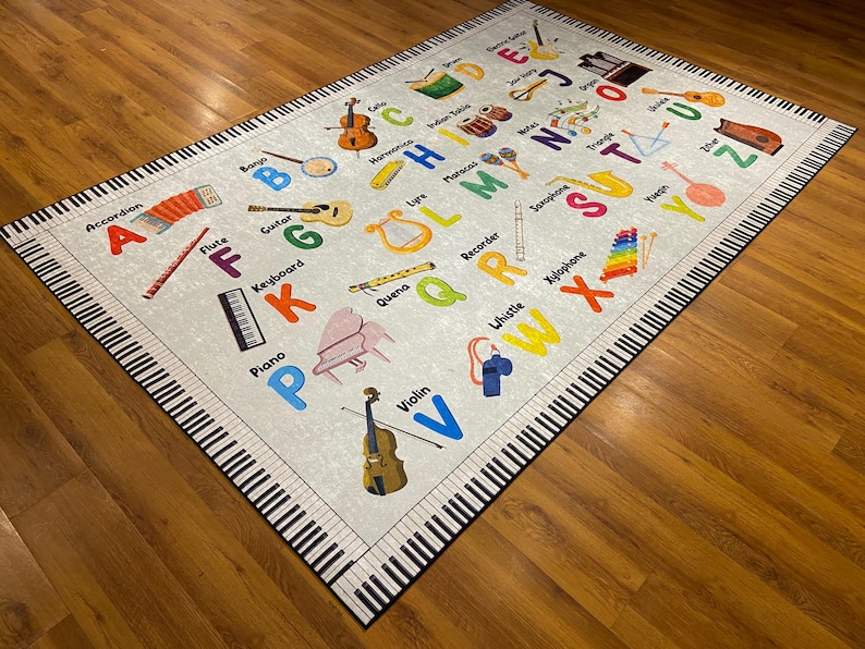 May include: A rectangular rug with a musical theme. The rug features a light gray background with colorful illustrations of musical instruments and the alphabet. The border of the rug is designed to look like piano keys.