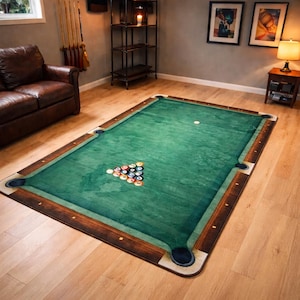 May include: A rectangular area rug designed to resemble a pool table. The rug features a green playing surface with brown wooden-look borders, corner pockets, and a rack of billiard balls. A white cue ball is also visible.