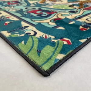 May include: Close-up of a decorative rug with a detailed pattern. The rug features a teal, green, and cream color scheme with a black border. The design includes floral and animal motifs.
