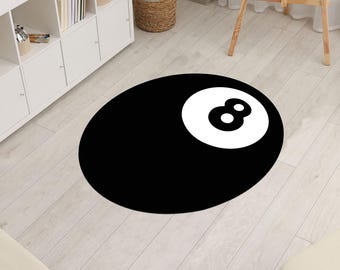 May include: A round black rug with a white number eight billiard ball design. The rug is placed on a light wood floor. The rug is a decorative item for a game room or living space.
