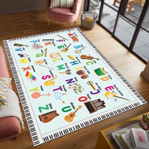 May include: A rectangular area rug with a light blue background features an alphabet with musical instruments. The rug's border is designed to look like piano keys. Instruments include a guitar, violin, drum, and ukulele.