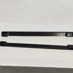 Puede incluir: Dos bridas de plástico negras, cada una con una pequeña cabeza rectangular en un extremo.