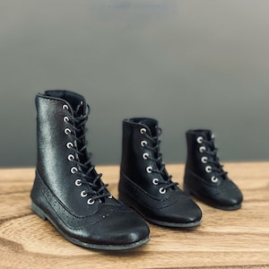 Op de afbeelding: Drie paar zwarte leren veterschoenen in verschillende maten. De schoenen hebben een ronde neus en een dikke hak.