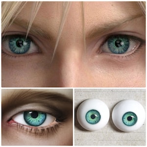 May include: Close-up of two realistic-looking green and blue doll eyes. The eyes are on a white surface.