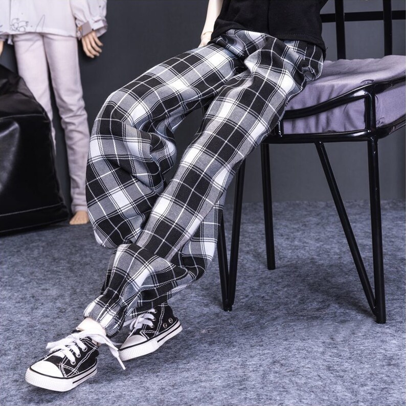 May include: Black and white plaid pants with a cuffed hem. The pants are worn by a person sitting on a black metal chair.