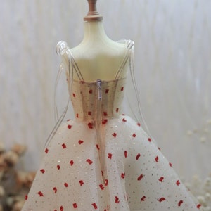 May include: A white tulle dress with red polka dots and a zipper closure in the back. The dress is on a white mannequin.