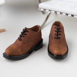 Puede incluir: Un par de zapatos marrones de cuero con cordones negros. Los zapatos tienen una punta redonda y una suela de goma negra.