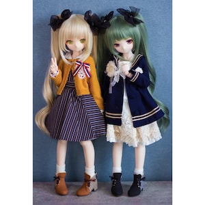 May include: Two dolls with long hair, one with blonde hair and a yellow sweater and striped skirt, the other with green hair and a navy blue jacket and white skirt. Both dolls are wearing black boots.