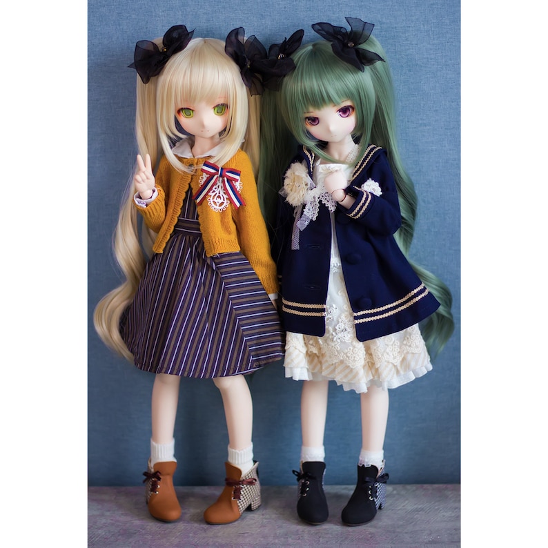 May include: Two dolls with long hair, one with blonde hair and a yellow sweater and striped skirt, the other with green hair and a navy blue jacket and white skirt. Both dolls are wearing black boots.