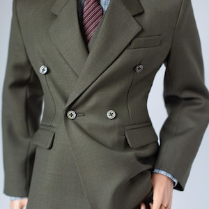 May include: A dark olive green double-breasted suit with matching trousers. The suit has a notched lapel, two rows of buttons, and a subtle textured weave. A striped burgundy tie and a blue and white checked shirt are visible.