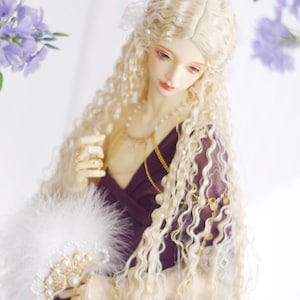 May include: A doll with long, curly blonde hair and a deep purple dress. The doll wears gold necklaces and holds a white feathered fan with pearl accents. The doll's face has delicate features and is adorned with makeup. The background includes purple flowers.