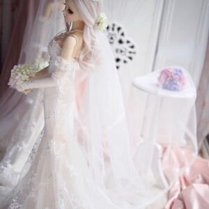 May include: A white bridal gown with lace detailing and a long veil. The gown has a sweetheart neckline and a fitted bodice. The bride is holding a bouquet of white flowers.