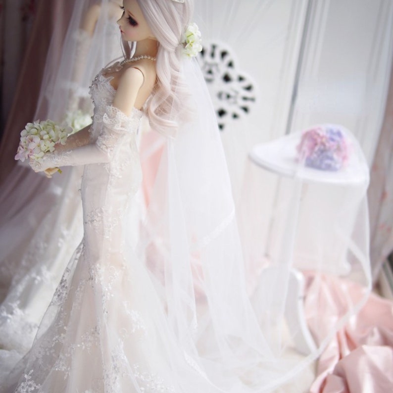 May include: A white bridal gown with lace detailing and a long veil. The gown has a sweetheart neckline and a fitted bodice. The bride is holding a bouquet of white flowers.