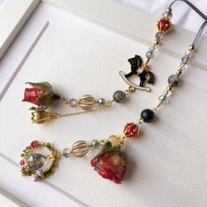 May include: A gold chain necklace with red and green floral accents, a black rocking horse charm, and clear and gray beads.
