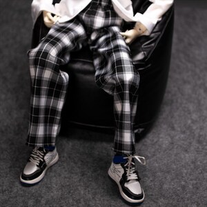 May include: Black and white plaid pants with a white shirt. The person is wearing white sneakers with black accents.