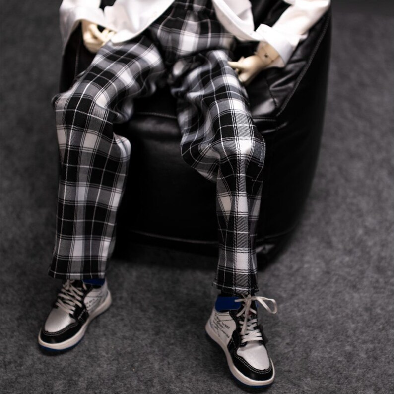 May include: Black and white plaid pants with a white shirt. The person is wearing white sneakers with black accents.