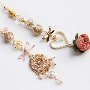 May include: Two delicate gold charm necklaces with pink and white beads, a heart charm, a rose charm, and a floral design charm.