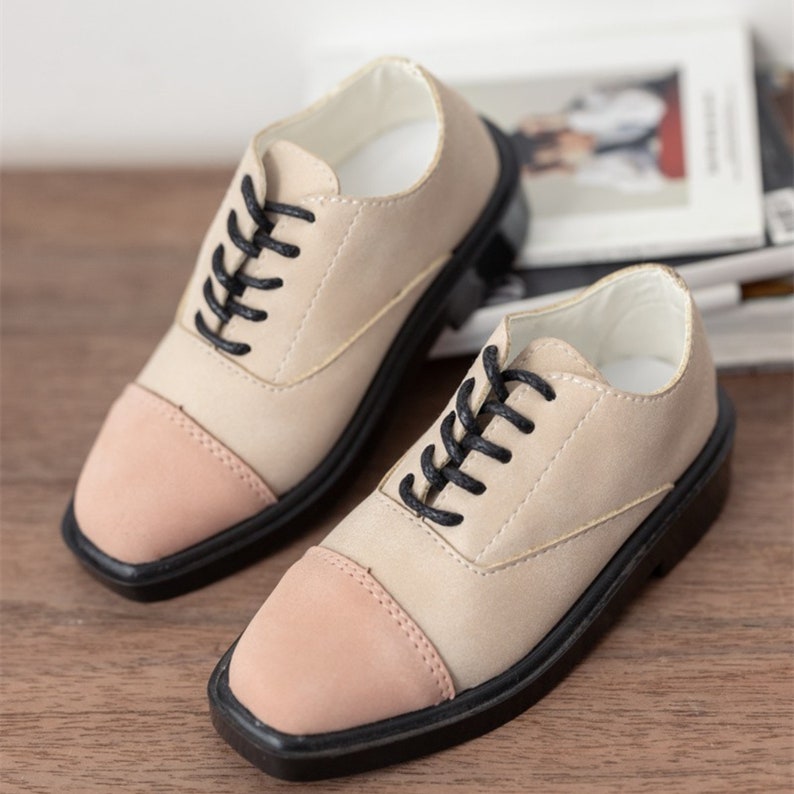 Puede incluir: Un par de zapatos de cordones beige y rosa con cordones negros y punta cuadrada.