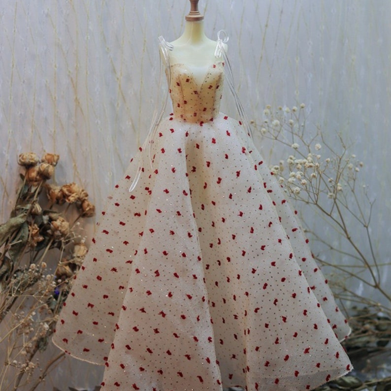 May include: A white tulle ball gown with red polka dots. The dress has a sweetheart neckline and thin straps.