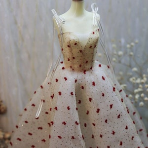 May include: A white tulle dress with red polka dots and a V-neckline. The dress has thin straps and a full skirt.
