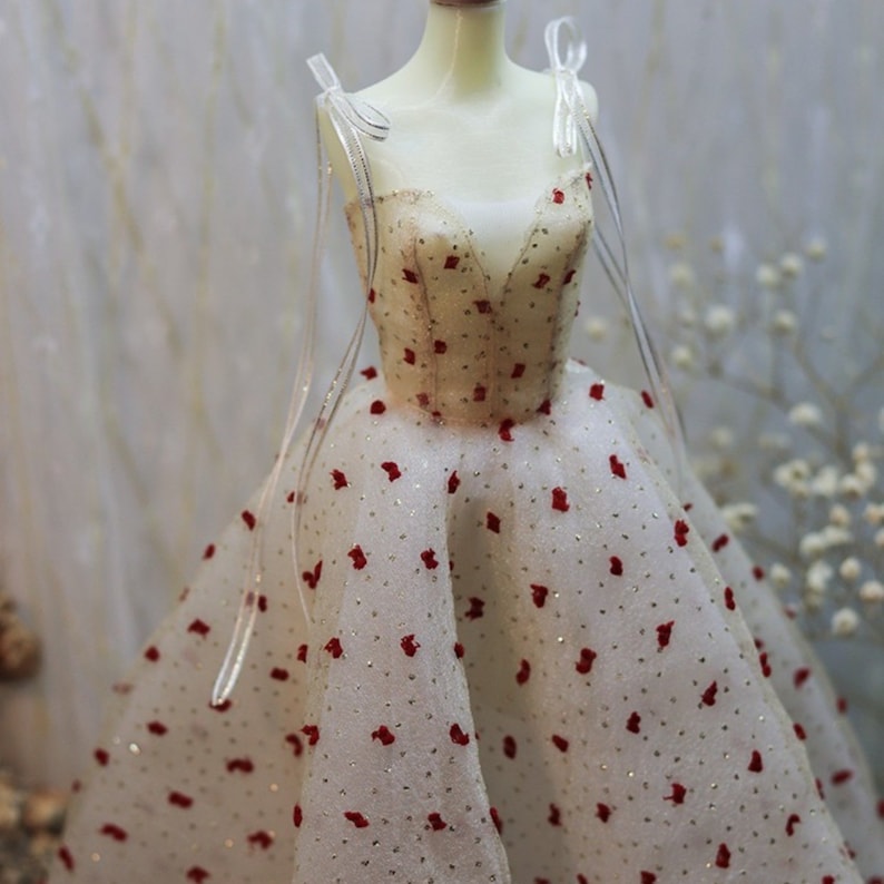 May include: A white tulle dress with red polka dots and a V-neckline. The dress has thin straps and a full skirt.