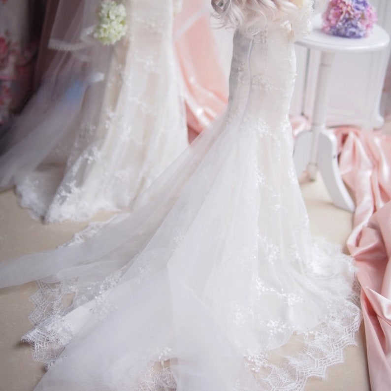 May include: Two white wedding dresses with lace detailing. One dress has a long train and the other has a shorter train.