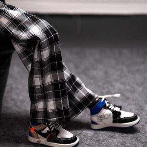 May include: A pair of black and white plaid pants with a white and black high-top sneaker with blue accents and the word "AIR" on the side.