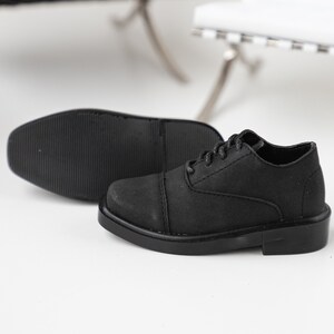 Puede incluir: Un par de zapatos negros de cuero con cordones, punta redonda y suela gruesa.
