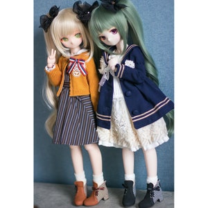 May include: Two dolls with long hair, one with blonde hair and a yellow cardigan and striped skirt, the other with green hair and a navy blue jacket with gold trim and a white lace skirt. Both dolls are wearing black boots.