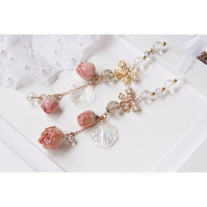 May include: Two delicate gold charm necklaces with pink dried flower accents, clear glass beads, and gold star and bow charms.