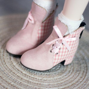 May include: A pair of pink ankle boots with white gingham fabric and pink laces. The boots have a rounded toe and a low heel.