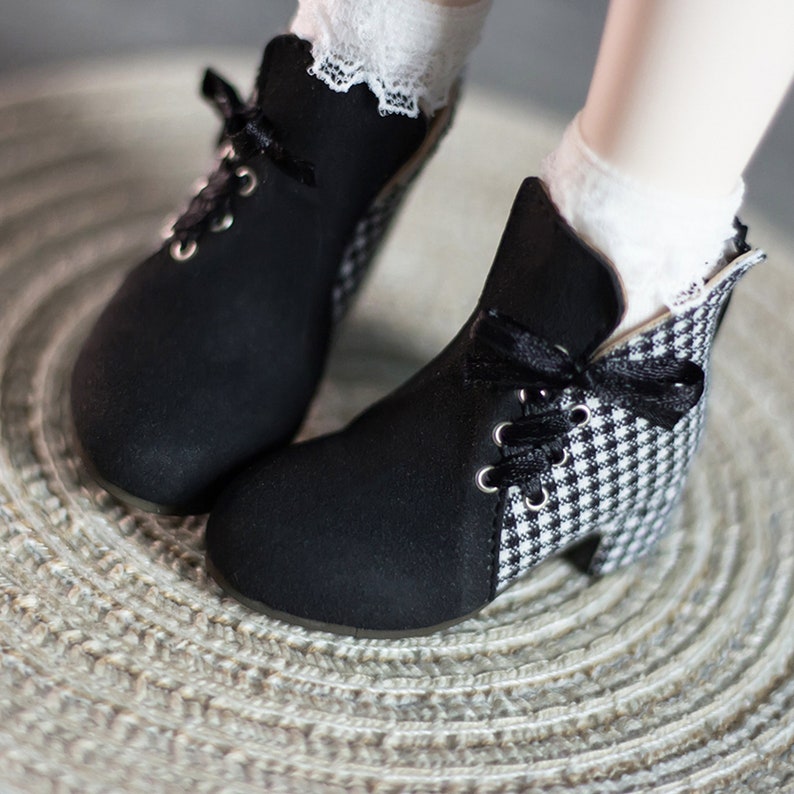 May include: Black ankle boots with a checkered pattern on the back of the heel. The boots have laces and a bow on the front.