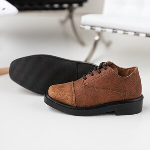 Puede incluir: Zapatos marrones de cuero con cordones y suela negra. Los zapatos tienen una parte superior de cuero texturizado y un estilo oxford cl&aacute;sico.