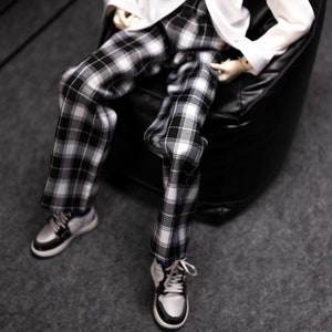 May include: A pair of black and white plaid pants with a white shirt. The pants are worn by a person sitting in a black beanbag chair.