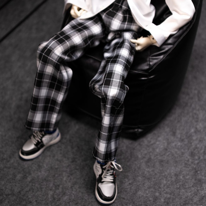 May include: A pair of black and white plaid pants with a white shirt. The pants are worn by a person sitting in a black beanbag chair.