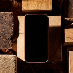 K&ouml;nnte beinhalten: Ein schwarzes Smartphone mit leerem Bildschirm liegt auf einer Holzoberfl&auml;che. Das Telefon ist von Holzst&uuml;cken umgeben.