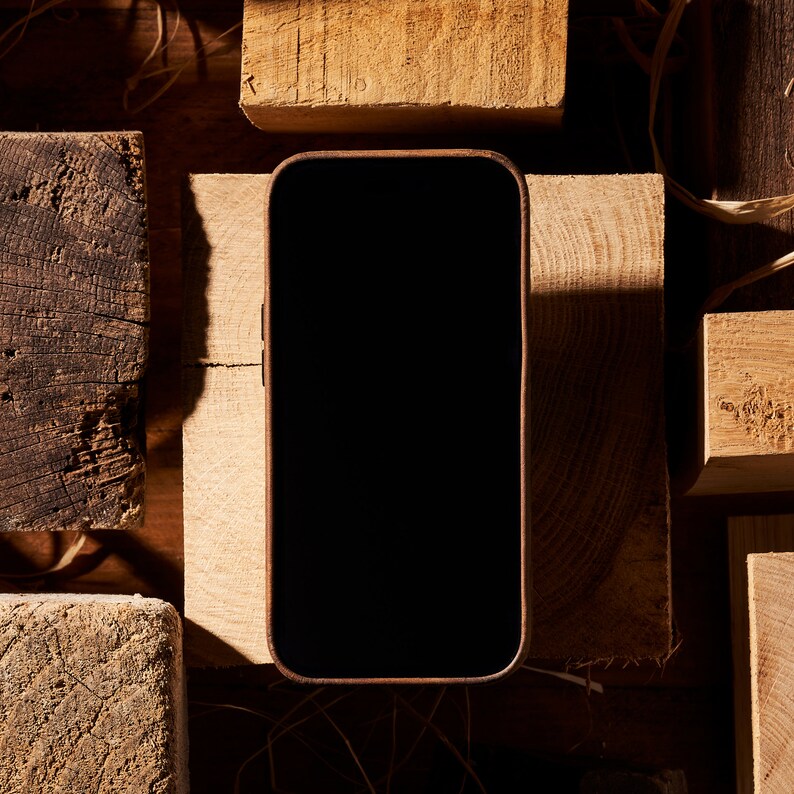 K&ouml;nnte beinhalten: Ein schwarzes Smartphone mit leerem Bildschirm liegt auf einer Holzoberfl&auml;che. Das Telefon ist von Holzst&uuml;cken umgeben.