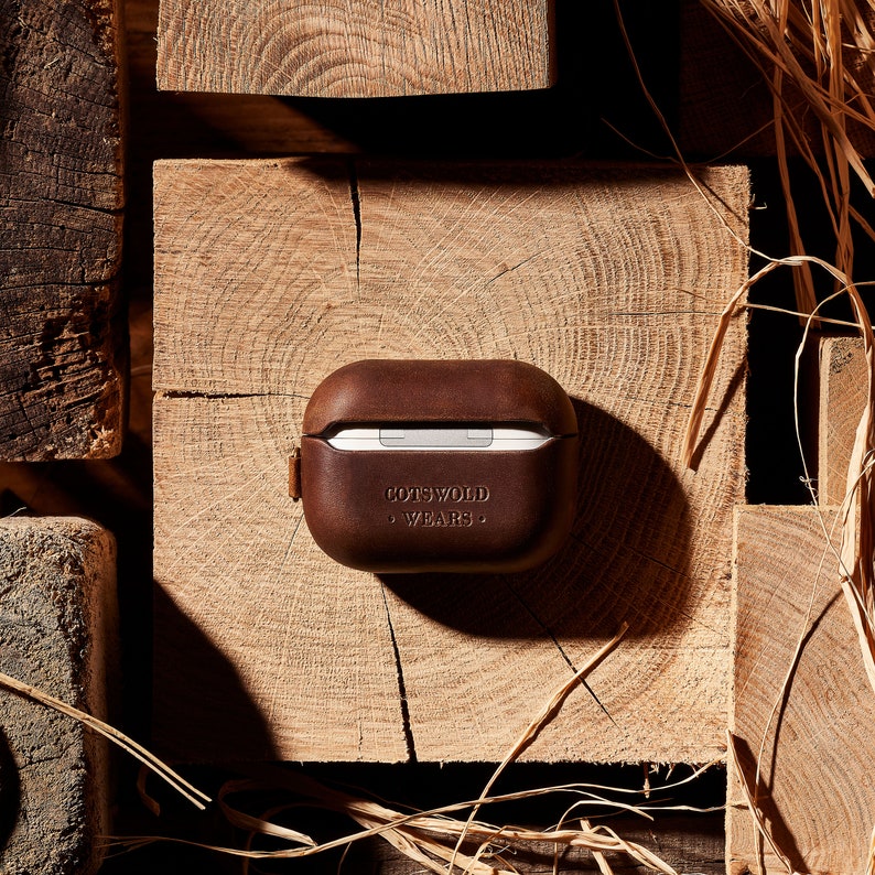 May include: A brown leather case for AirPods with the text "Cotswold Wears" embossed on the front.