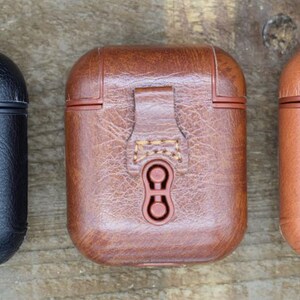 May include: Three leather cases for wireless earbuds in black, brown, and tan. Each case has a flap with a snap closure and a small loop.
