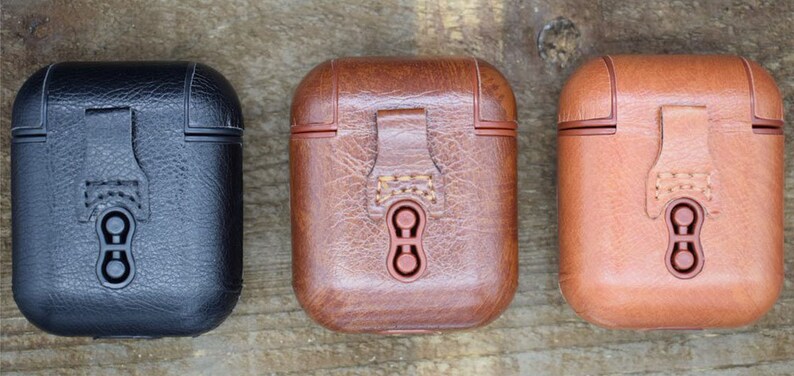 May include: Three leather cases for wireless earbuds in black, brown, and tan. Each case has a flap with a snap closure and a small loop.