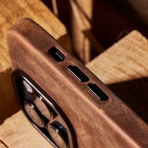 K&ouml;nnte beinhalten: Eine braune Leder-Handyh&uuml;lle mit Ausschnitten f&uuml;r die Kamera und die Tasten. Die H&uuml;lle hat einen abgenutzten, verwitterten Look.