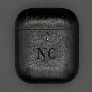 May include: Black leather case for wireless earbuds with the initials "NC" embossed on the front.