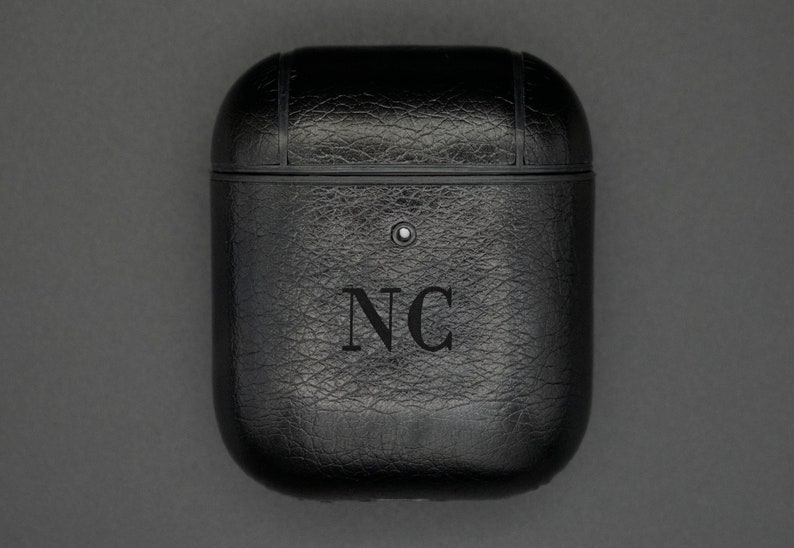 May include: Black leather case for wireless earbuds with the initials "NC" embossed on the front.