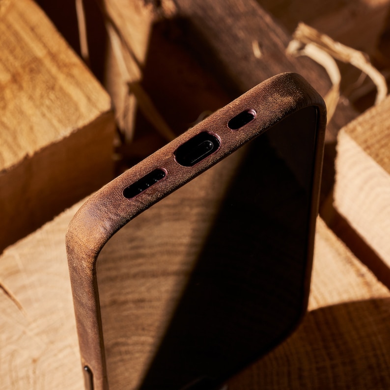 K&ouml;nnte beinhalten: Eine braune Holz Handyh&uuml;lle mit Ausschnitten f&uuml;r die Kamera und den Ladeanschluss.