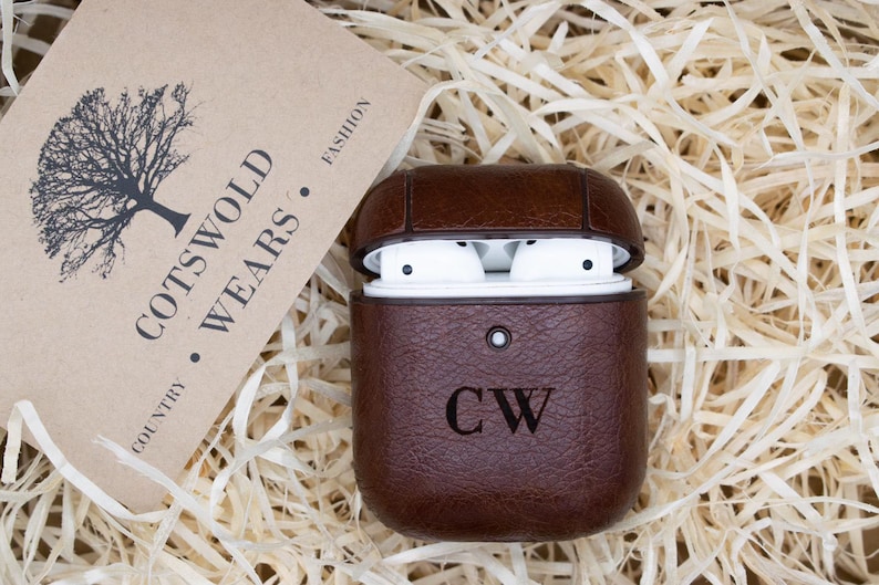 May include: Brown leather case for Apple AirPods with the initials "CW" embossed on the front. The case is open, revealing the white AirPods inside.