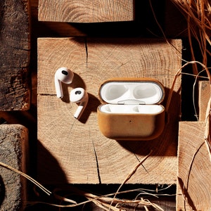 May include: A brown leather case for wireless earbuds with two white earbuds sitting next to it on a wooden surface.