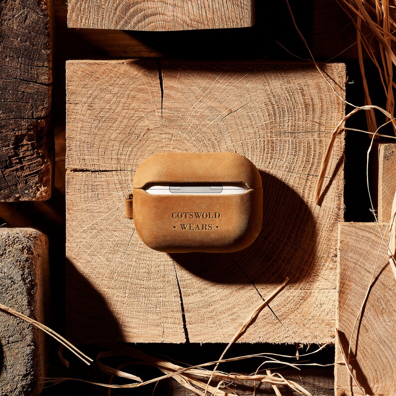 May include: A brown leather case for AirPods with the text "Cotswold Wears" embossed on the front.